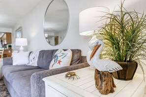 Un salon avec un canapé gris, une table basse blanche, un grand miroir et une plante en pot.