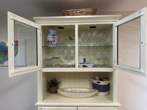 Un meuble blanc aux portes vitrées, contenant de la verrerie, un vase décoratif et un panier en osier posé sur le dessus.