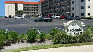 A multi-story hotel with a parking lot, a sign indicating the address, and a view of the ocean.
