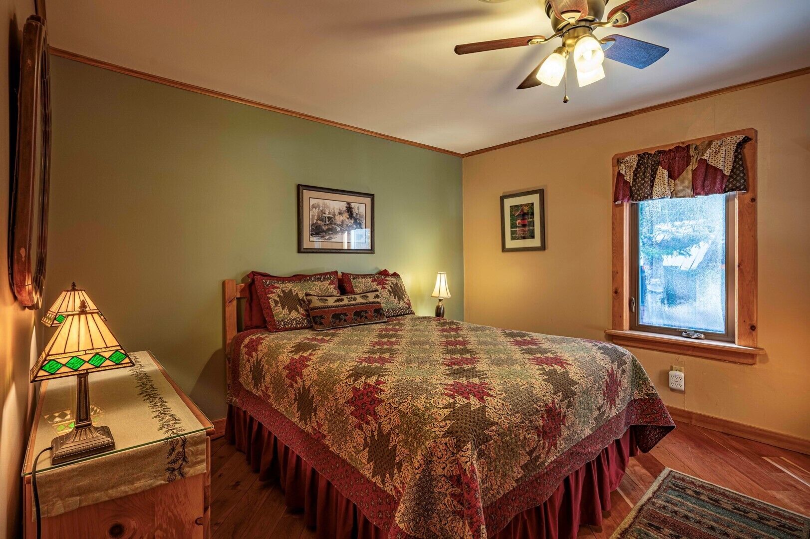 A bedroom with a bed, a nightstand, a lamp, a ceiling fan, and a window with curtains.