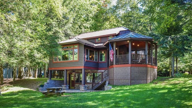 A two-story house with a covered porch, a stone foundation, and a flag. - Historic Highland Cottage - 4th Lake (Inlet)