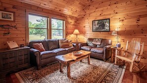 L’intérieur chaleureux d’un chalet avec un plafond en bois, des canapés en cuir, une table basse en bois et un fauteuil à bascule.