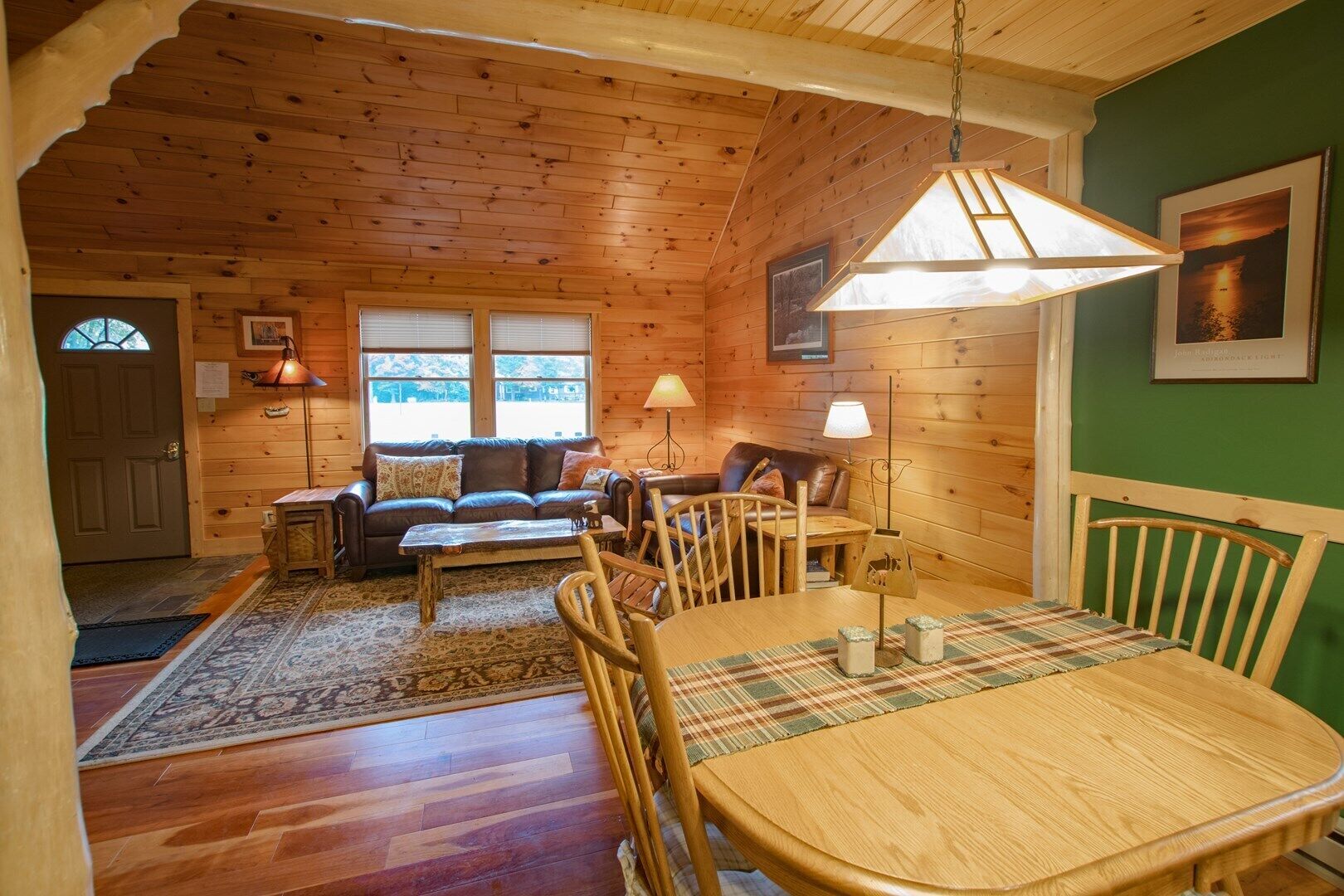 A cozy cabin interior with a wooden dining table, a sofa, and a lamp.