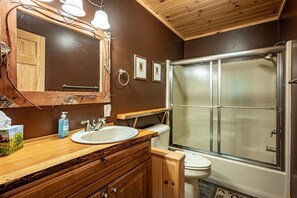 Een badkamer met een houten wastafelmeubel, twee wastafels, een spiegel, een toilet en een douchecabine met glazen wanden.
