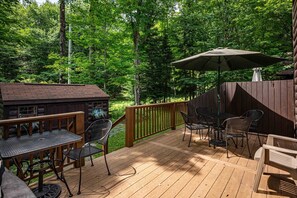 Een houten terras met tuinmeubilair, waaronder een tafel en stoelen, en een houten chalet op de achtergrond.