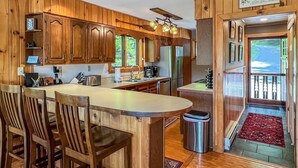 L’intérieur d’un chalet en bois comprend un espace cuisine avec un îlot central, des tabourets de bar et une poubelle.