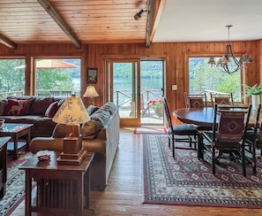 Un intérieur de chalet chaleureux comprenant un espace de vie, un coin repas et de grandes fenêtres donnant sur un paysage naturel.