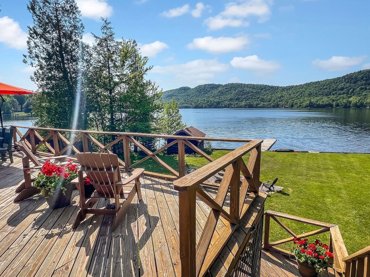 A wooden deck with a view of a lake and hills, featuring a chair and a flower pot.