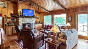 Une chambre confortable, aménagée dans le style d’un chalet, avec une cheminée en pierre, des meubles en bois et de grandes fenêtres offrant une vue sur l’extérieur.