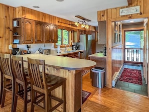 Un intérieur en bois comprenant un espace cuisine, un coin repas et une vue sur l’extérieur, visible à travers une porte.