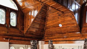 A wooden cabin bedroom with a large bed, two windows with curtains, and a sloped ceiling. - Ketav's Ayush Health Paradise (Palampur)