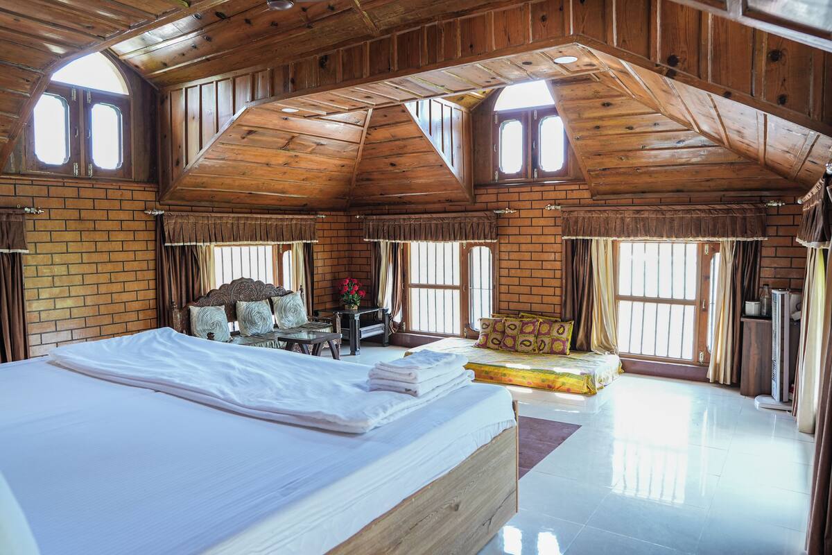 Een ruime slaapkamer met een groot bed, een houten plafond en meerdere ramen.