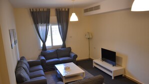 A modern living room with a sofa set, a coffee table, a flat-screen TV on a stand, and a floor lamp. - Arman Hotel Suites (Amman)