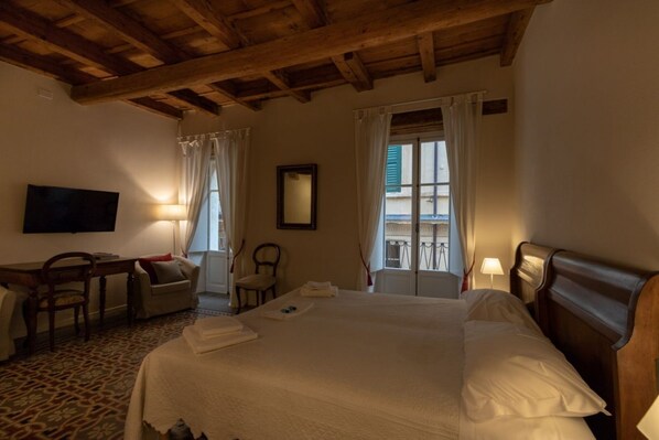 A hotel room with a large bed, a desk with a chair, a television, and two windows with curtains.