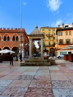 A plaza with a central fountain, surrounded by historic buildings with arched windows and a red brick facade. - Cappello 1 near the Arena and the Balcony of Juliette and the Arena (Verona)