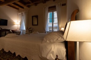Un dormitorio con cama, cabecera de madera, mesita de noche, lámpara, silla y ventana con cortinas.