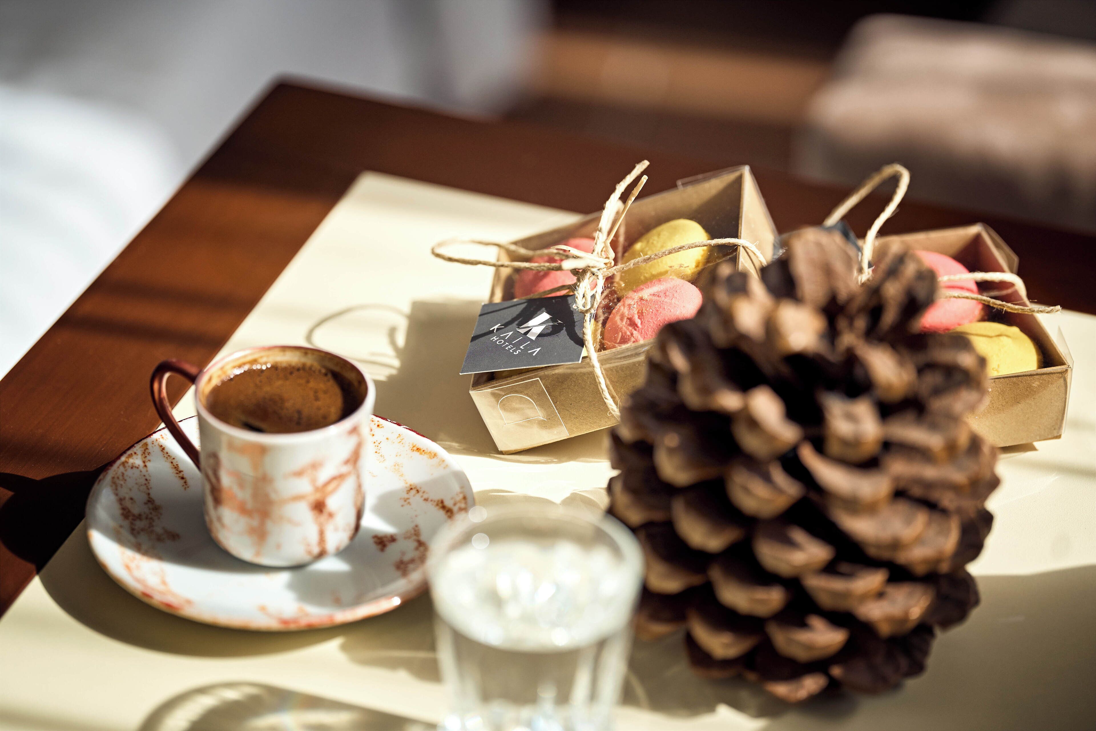 Een tafel met een koffiekop, een glas water, een dennenappel en cadeauverpakkingen.