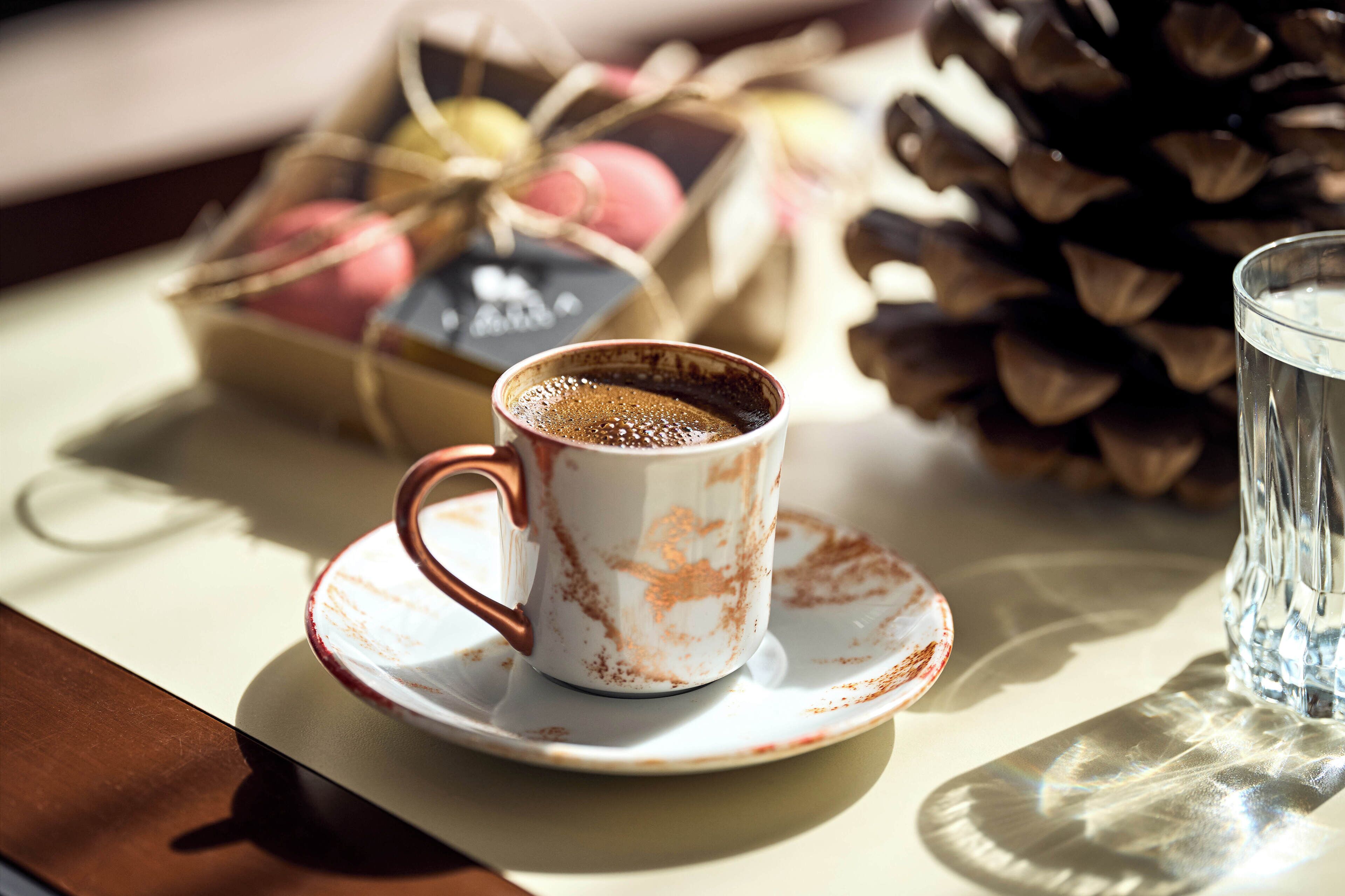 A cup of coffee on a saucer, a glass of water, and a basket of colorful macarons.