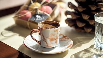 A cup of coffee on a saucer, a glass of water, and a basket of colorful macarons.