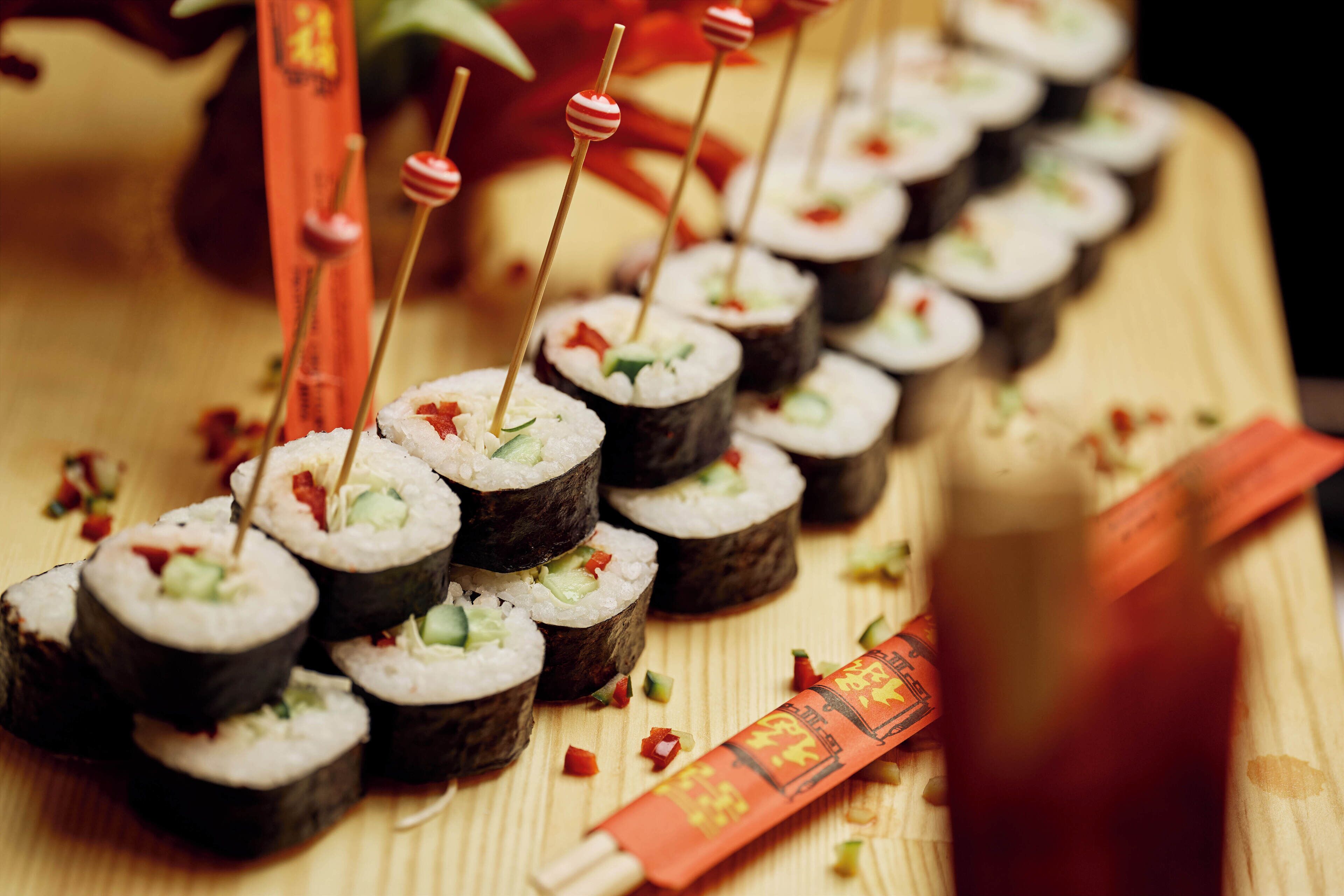 Sushi-rullat on aseteltu puupinnalla, ja niiden kanssa on syömäpuikot sekä koriste-elementtejä.