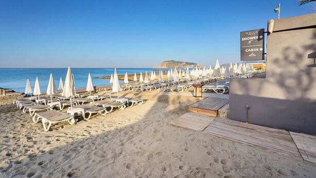 A beachside hotel with rows of sun loungers and umbrellas, a wooden deck, and a sign indicating a shower and cabin. - Kaila City Hotel (Alanya)