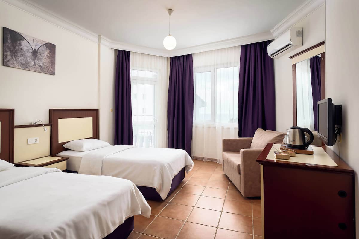 A hotel room with two beds, a desk with a kettle, a chair, and a TV.
