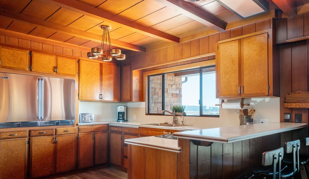 A modern kitchen with wooden cabinets, a large island with bar stools, and a stone backsplash.