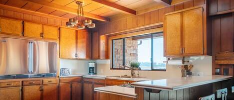 A modern kitchen with wooden cabinets, a large island with bar stools, and a stone backsplash.