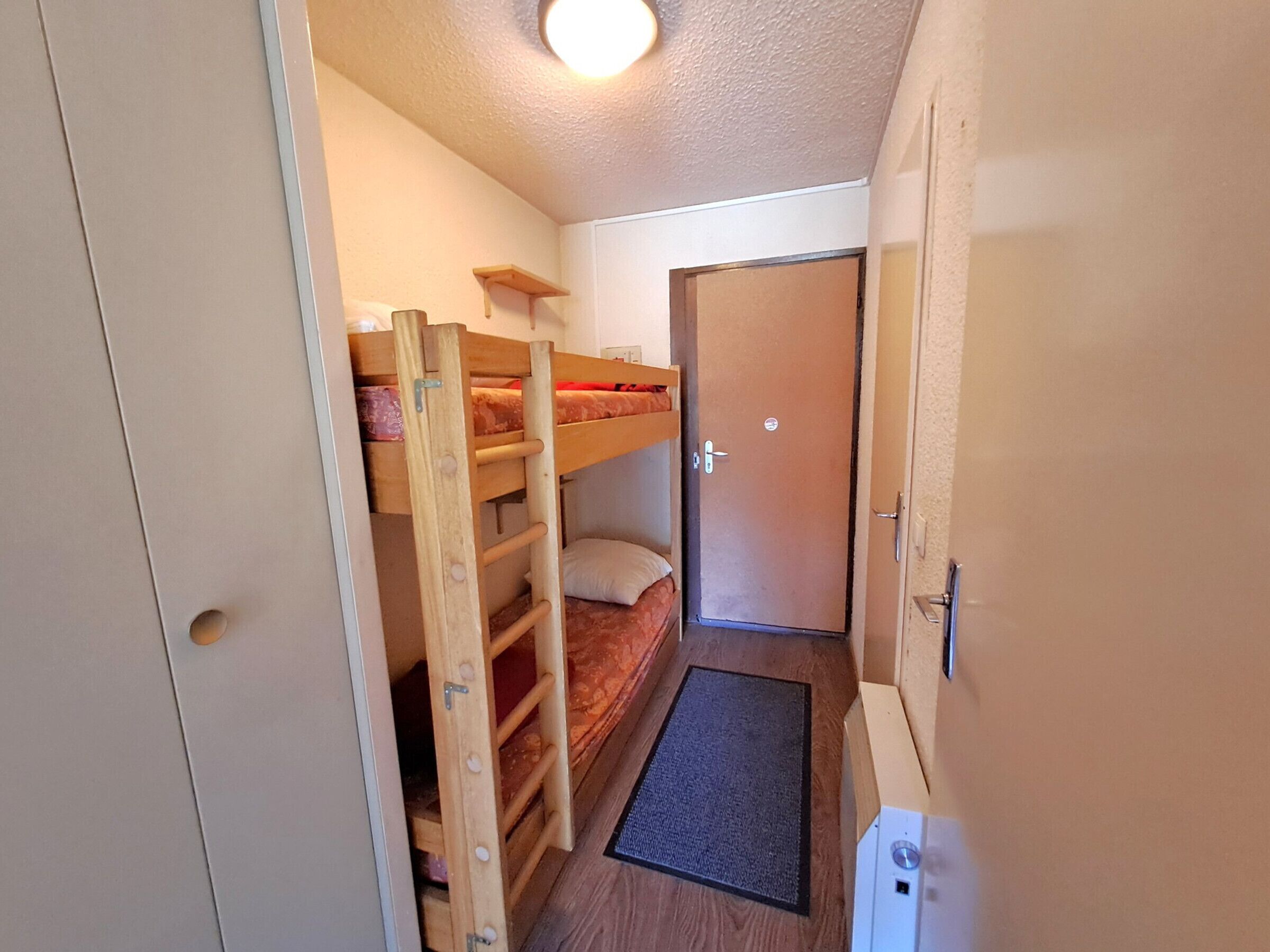 A small room with a bunk bed, a door, and a white cabinet.