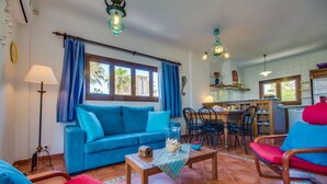 Una sala de estar con un sofá azul, sillas rojas, una mesa de comedor y una zona de cocina con ventanal.
