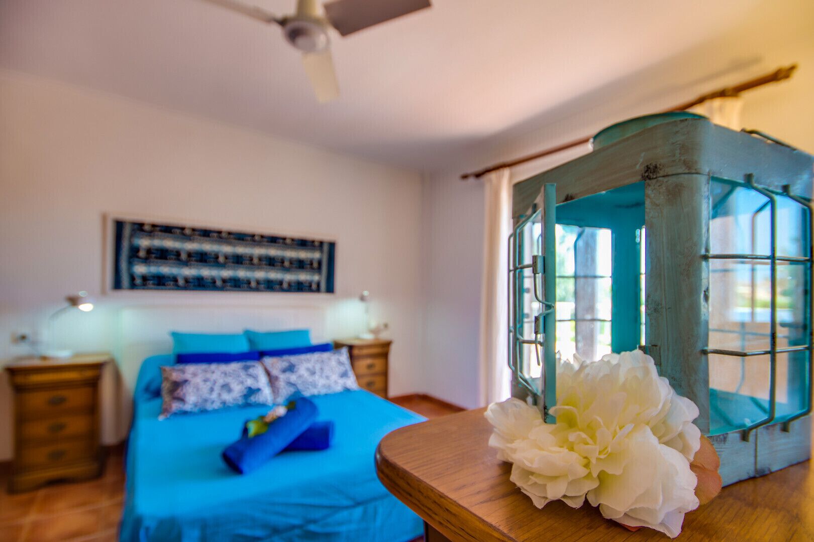 Une chambre à coucher comprenant un lit, une table de chevet, une lampe, un ventilateur de plafond et une fenêtre donnant sur un beau paysage.