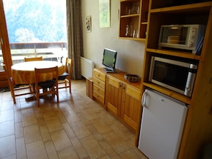 Eine kompakte Küche mit Holzschränken, einer Mikrowelle, einem Kühlschrank und einem Essbereich mit Tisch und Stühlen.