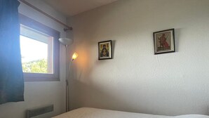 A bedroom with a bed, a window with curtains, a standing lamp, and two framed pictures on the wall. - Cozy apartment in Méribel for 4 pers., close to amenities (Méribel)