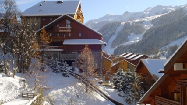 A mountain lodge with a snow-covered roof, wooden exterior, and a view of snow-covered mountains. - Cozy apartment in Méribel for 4 pers., close to amenities (Méribel)