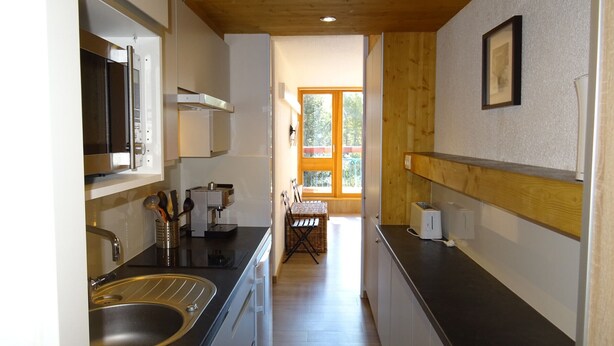 Eine kleine Küche mit Spüle aus Edelstahl, einer Mikrowelle und einem Toaster. Eine Holzdecke und ein Fenster sorgen für natürliches Licht.