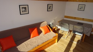 Ein gemütliches Zimmer mit einer Holzsofa, einem kleinen Tisch mit einem Tischleinenschal in Punkteoptik und einem Sessel. An den Wänden befinden sich Bilder in Rahmen.