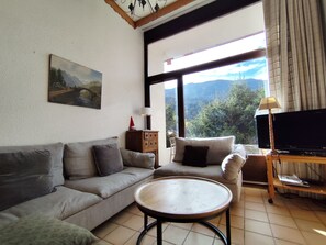A living room with a sofa, a coffee table, a TV on a stand, a lamp, and a painting on the wall.