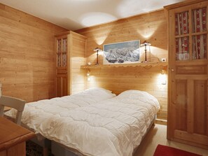 A wooden cabin bedroom with a bed, a nightstand, a lamp, and a painting on the wall.