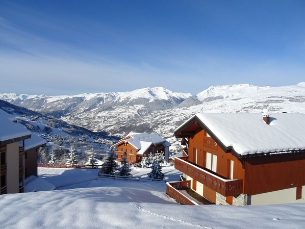 A snow-covered mountain village with wooden buildings and a clear view of snow-capped peaks in the background.