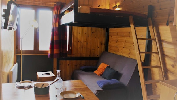 Interior acogedor de una cabaña con literas, un sofá, una mesa de comedor y una escalera.