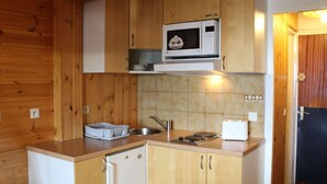 Cocina compacta con armarios de madera, microondas, refrigerador pequeño y lavamanos.