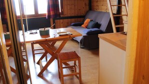Interior acogedor de una cabaña con una mesa de comedor de madera, un sofá y una escalera contra la pared.