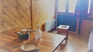 Un interior de madera con una mesa dispuesta para comer, un televisor montado en la pared y una ventana con cortinas.