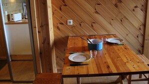 Una mesa de comedor de madera con platos, un vaso y una olla azul en una cocina con paredes de madera y un enchufe visible.