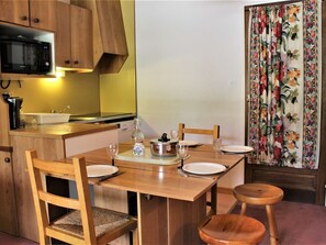 Cocina compacta con armarios de madera, microondas, lavamanos y una mesa de comedor preparada para cuatro comensales.