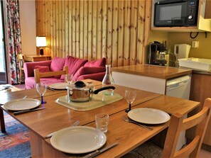 Uma área de refeições com uma mesa de madeira posta para dois, um micro-ondas sobre a bancada e uma cozinha compacta ao fundo.