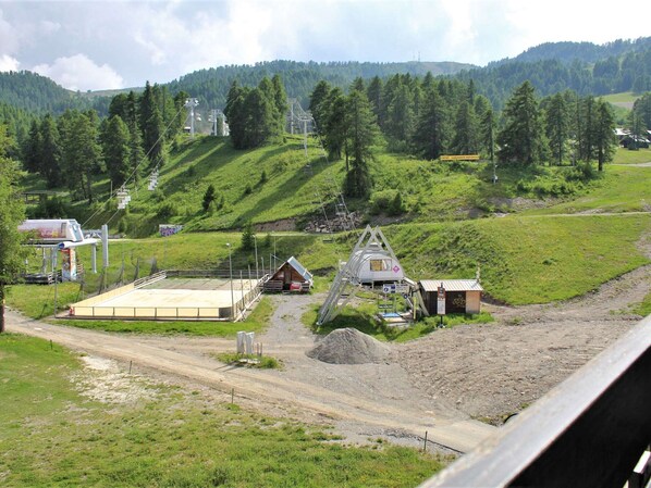 A rural landscape with a small building, a dirt road, and a forested hill in the background.