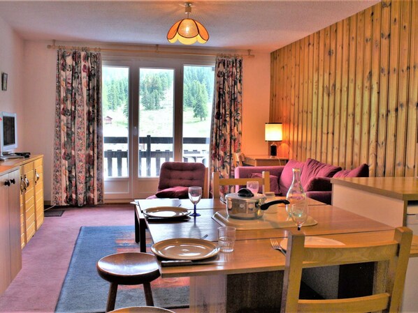 Una habitación acogedora con una mesa de comedor preparada para dos personas, un sofá, un aparador de madera y un televisor.
