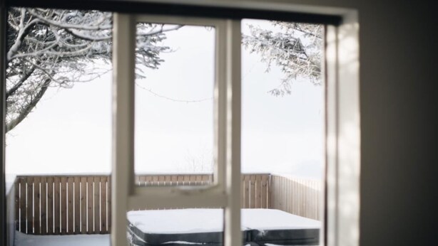 Una ventana con vistas a una terraza cubierta de nieve y una valla de madera.