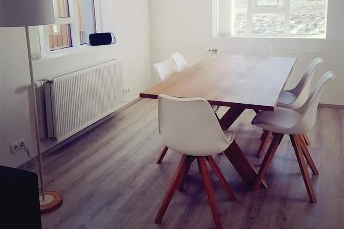 Un espace repas moderne avec une table en bois et des chaises blanches, un luminaire suspendu et une vue sur un paysage enneigé par de grandes fenêtres.